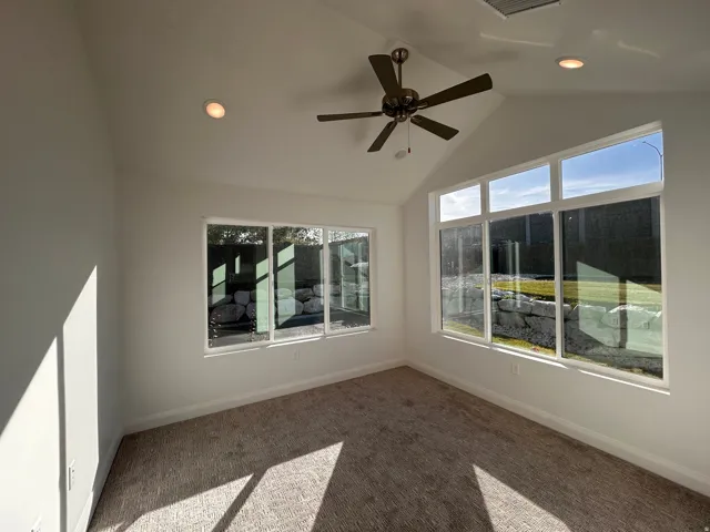 Carpeted spare room featuring healthy amount of natural light, lofted ceiling, a ceiling fan, and recessed lighting