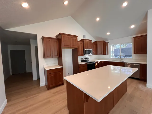 Kitchen with stainless steel appliances, a center island, light wood-type flooring, brown cabinetry, and recessed lighting