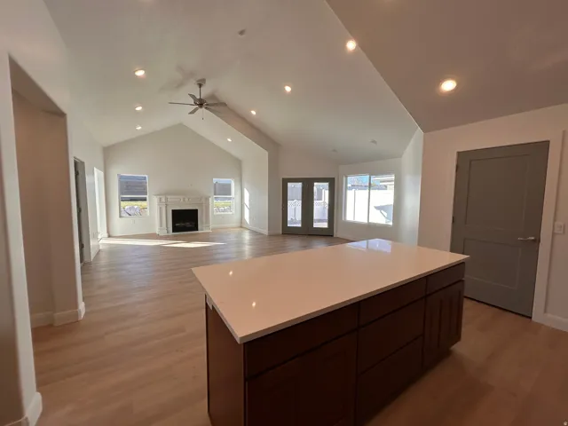 Kitchen featuring light wood-style flooring, light countertops, dark brown cabinetry, high vaulted ceiling, and open floor plan