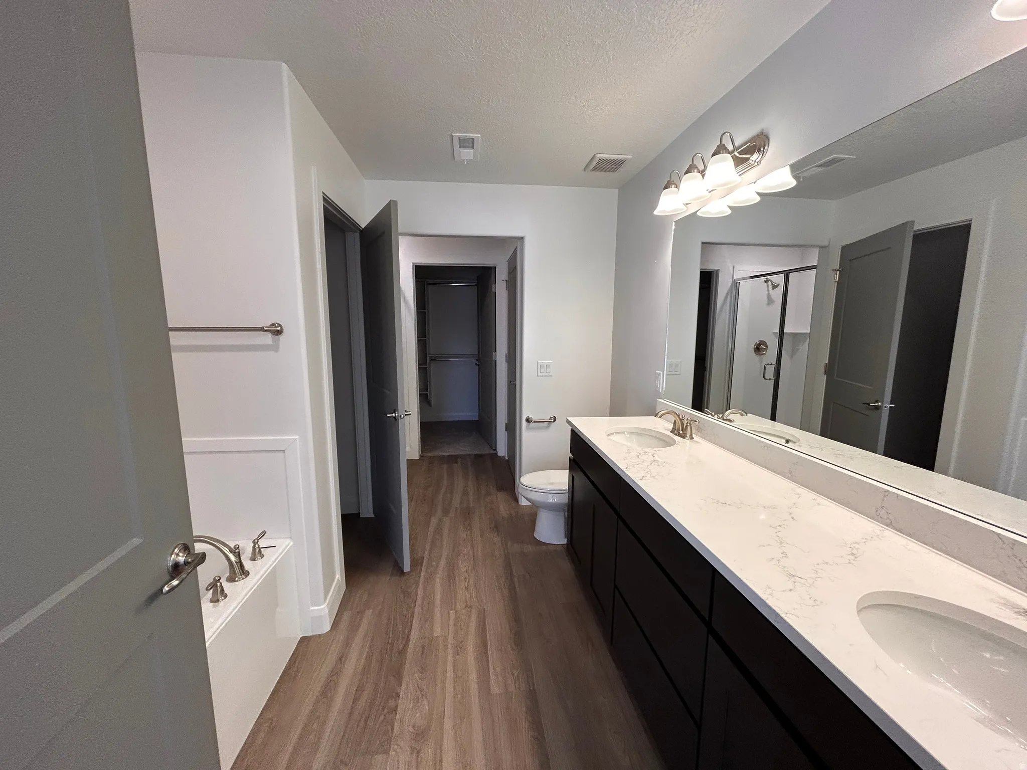 Full bath featuring dark wood-style floors, a stall shower, double vanity, a spacious closet, and a textured ceiling