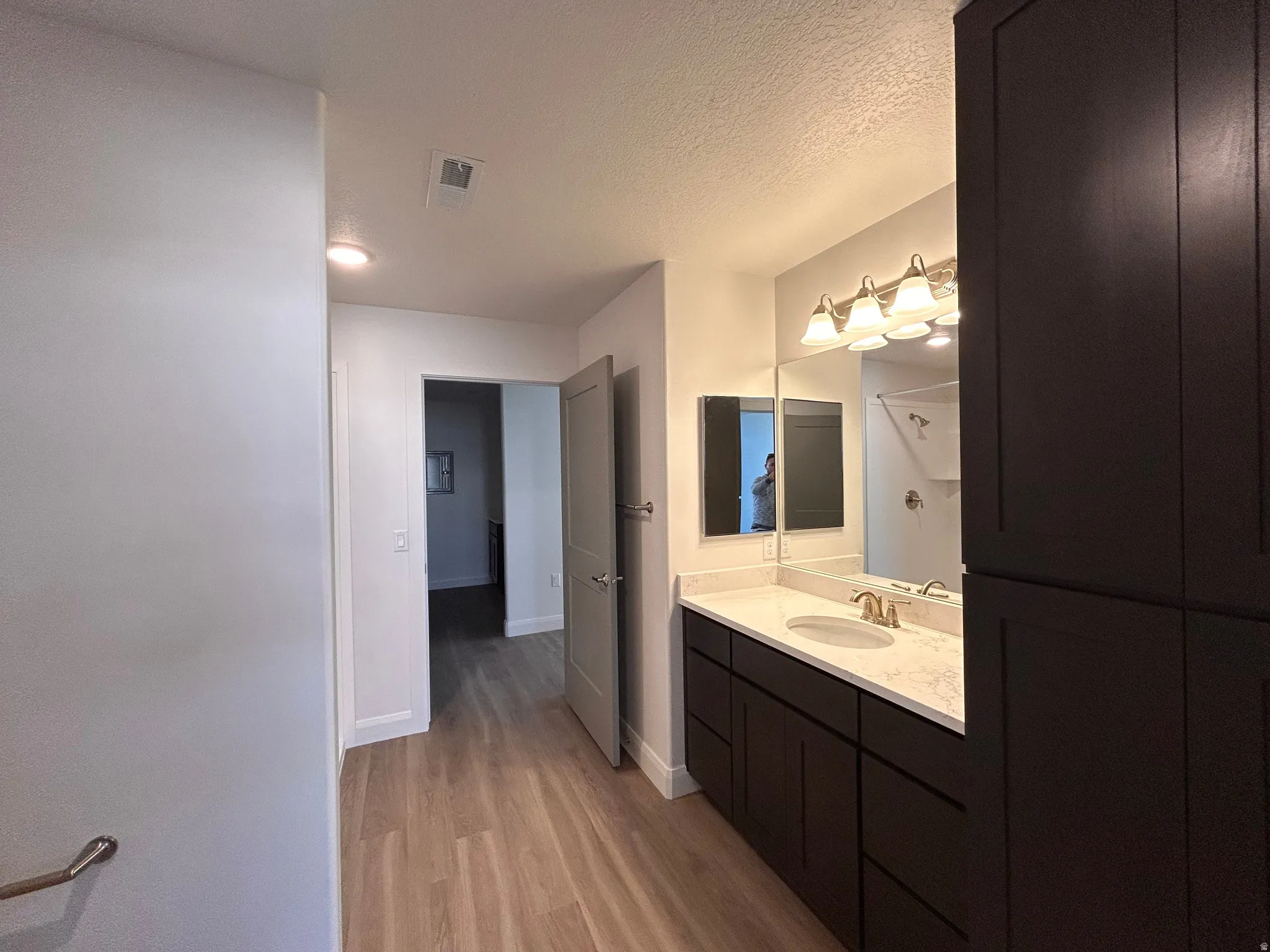 Bathroom with vanity, light wood-type flooring, a textured ceiling, and a shower