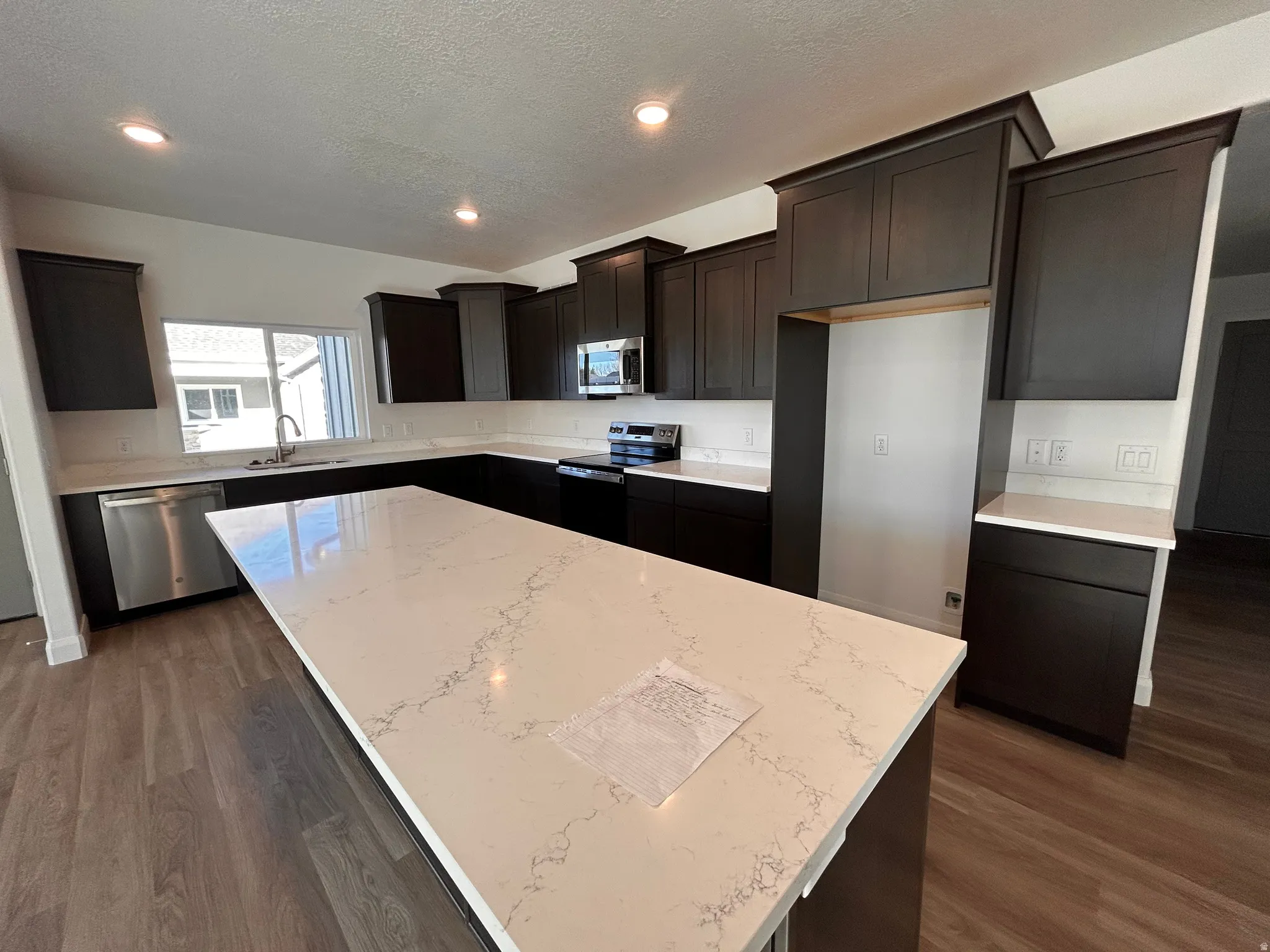 Kitchen with a center island, stainless steel appliances, a textured ceiling, light stone counters, and dark wood-type flooring