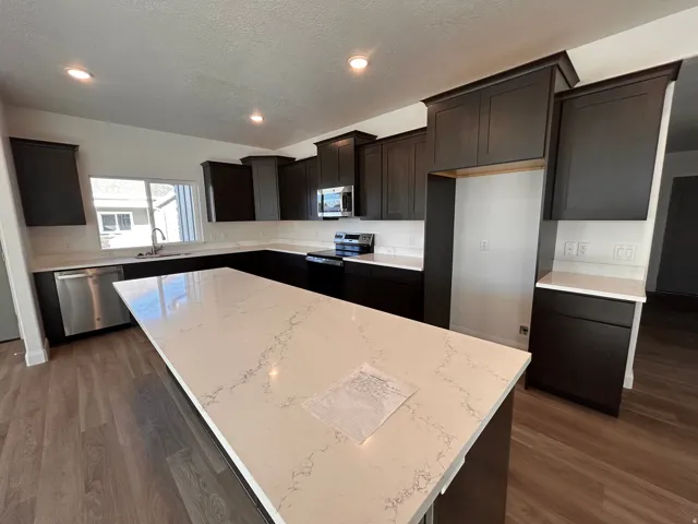 Kitchen with a center island, stainless steel appliances, a textured ceiling, light stone counters, and dark wood-type flooring