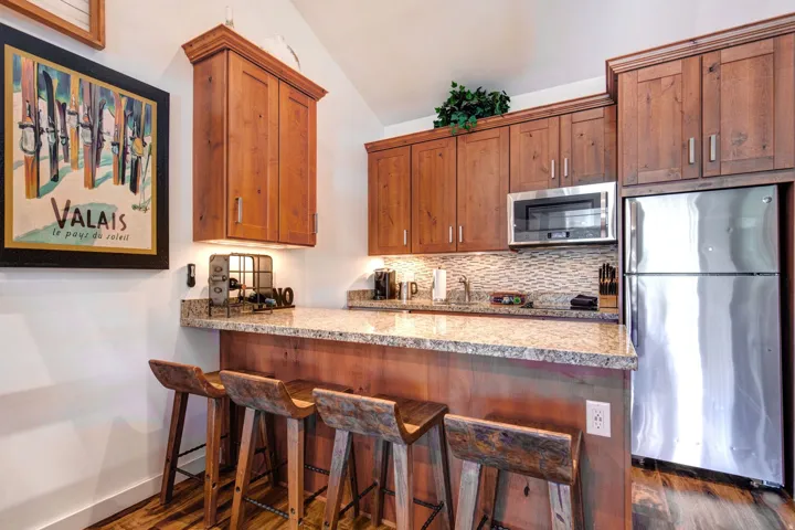 Kitchen with stainless steel appliances, decorative backsplash, light stone countertops, brown cabinets, and a breakfast bar area