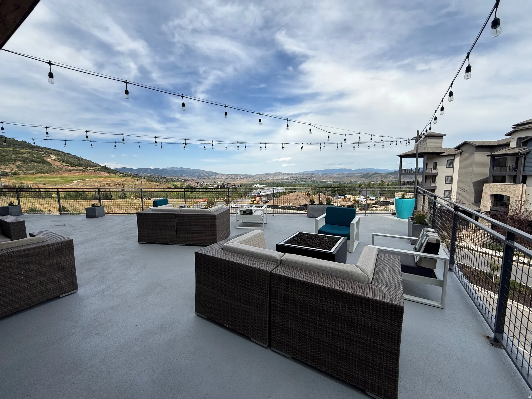 Spacious outdoor terrace with string lighting, metal railing, and panoramic mountain scenery