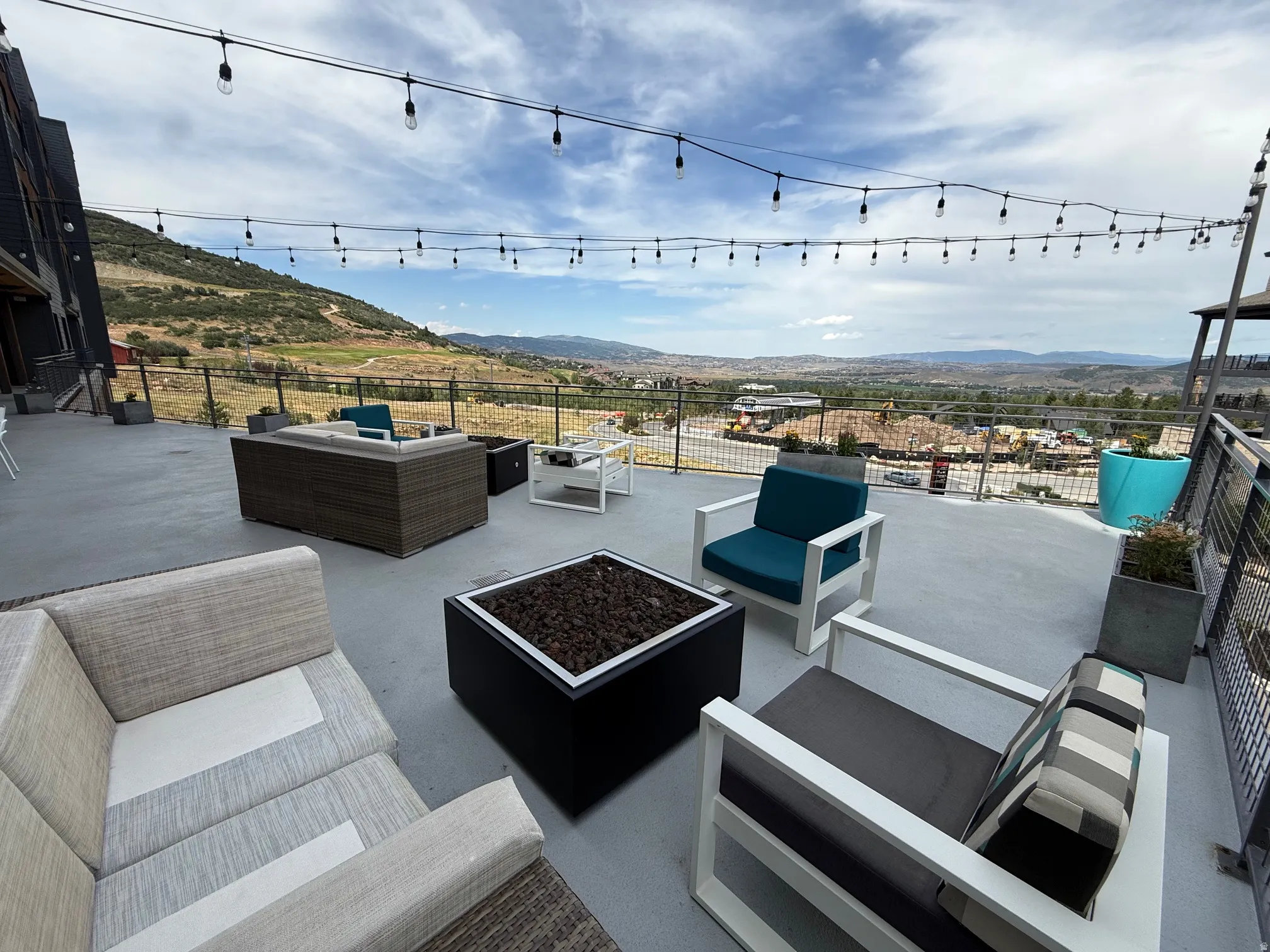 Expansive rooftop deck featuring string lighting, a gas fire pit, and a metal guardrail