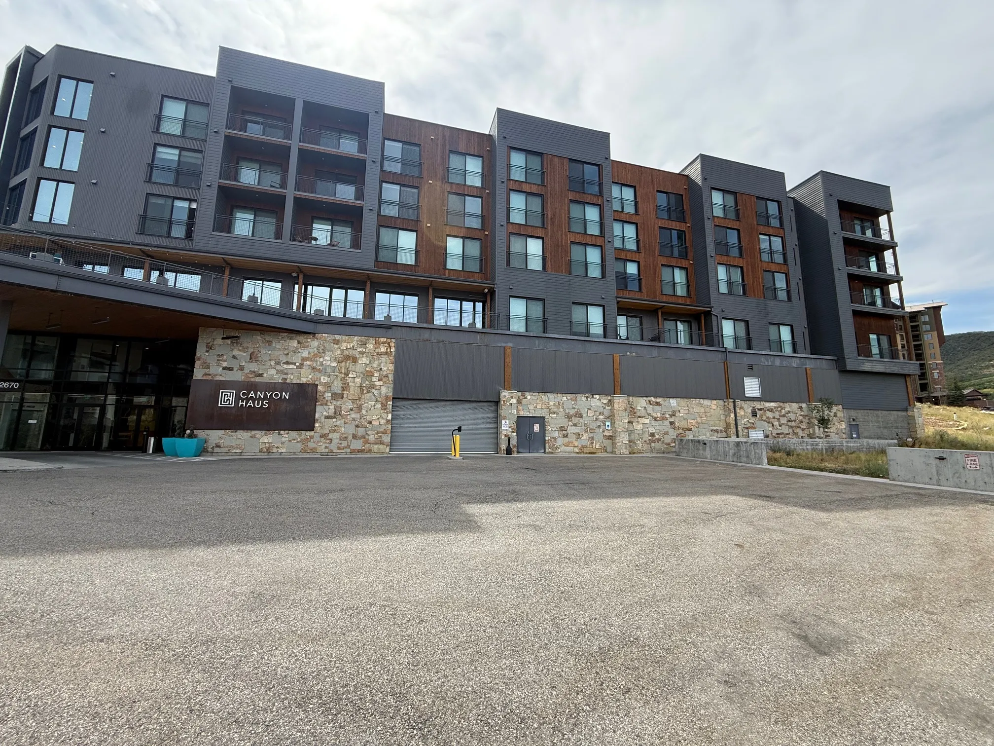 Contemporary building facade featuring a stone veneer base, dark gray paneling, and wood-finish accents