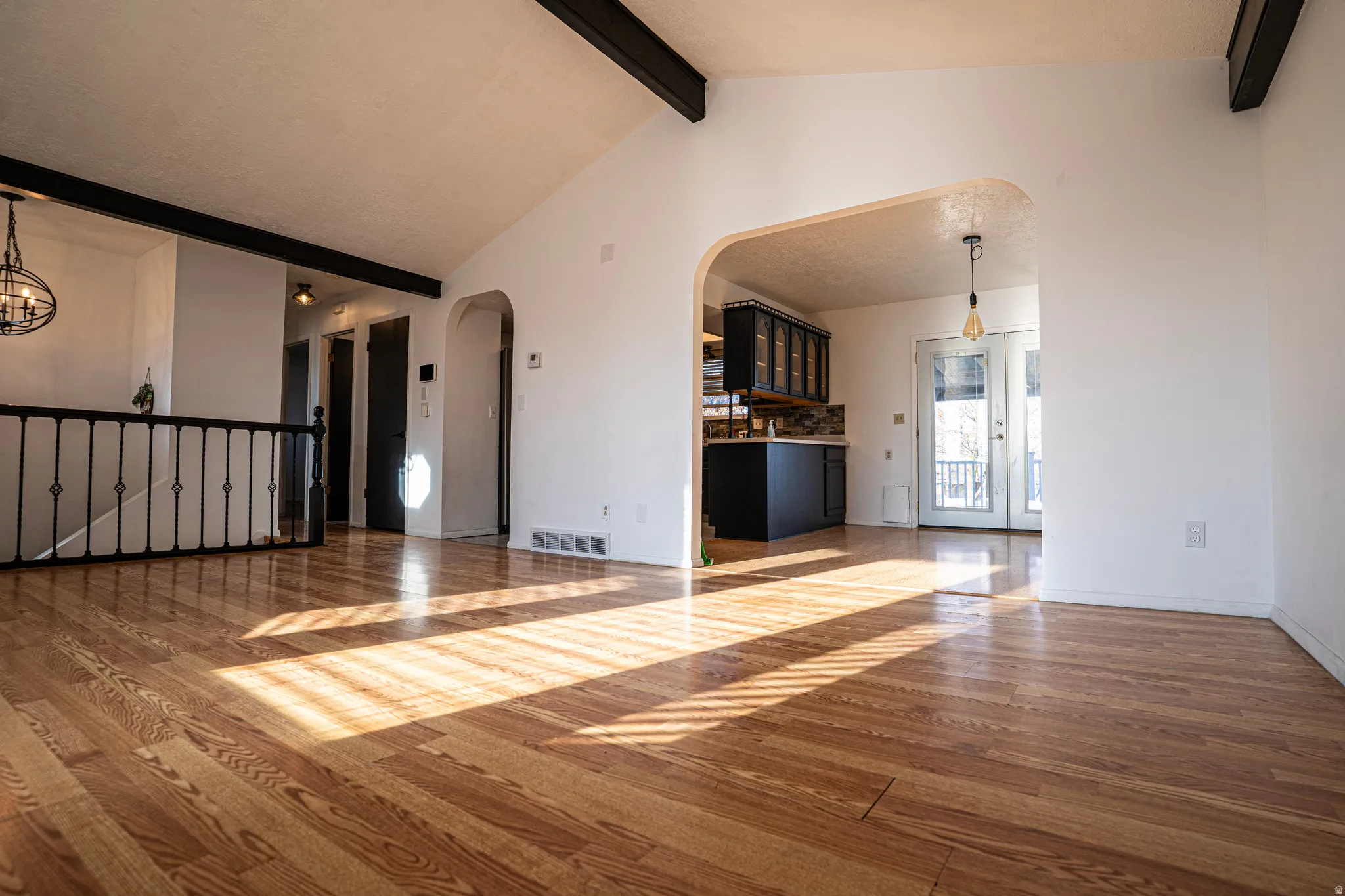 Unfurnished living room featuring hardwood / wood-style flooring, beam ceiling, arched walkways, and high vaulted ceiling