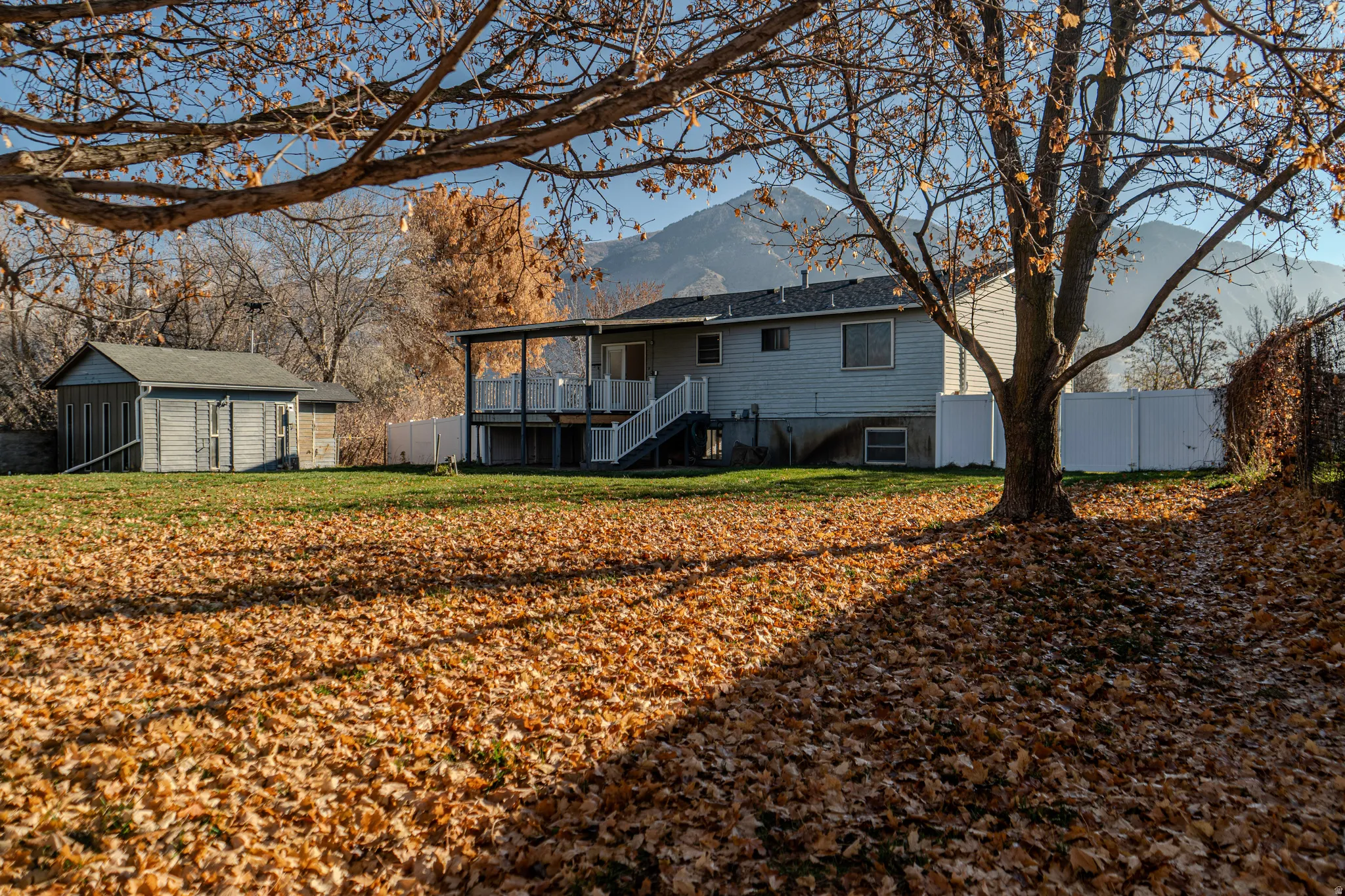 Rear view of house featuring stairway, a fully fenced backyard, full landscaping with fall leaves, a deck with mountain view, and a workshop outbuilding.