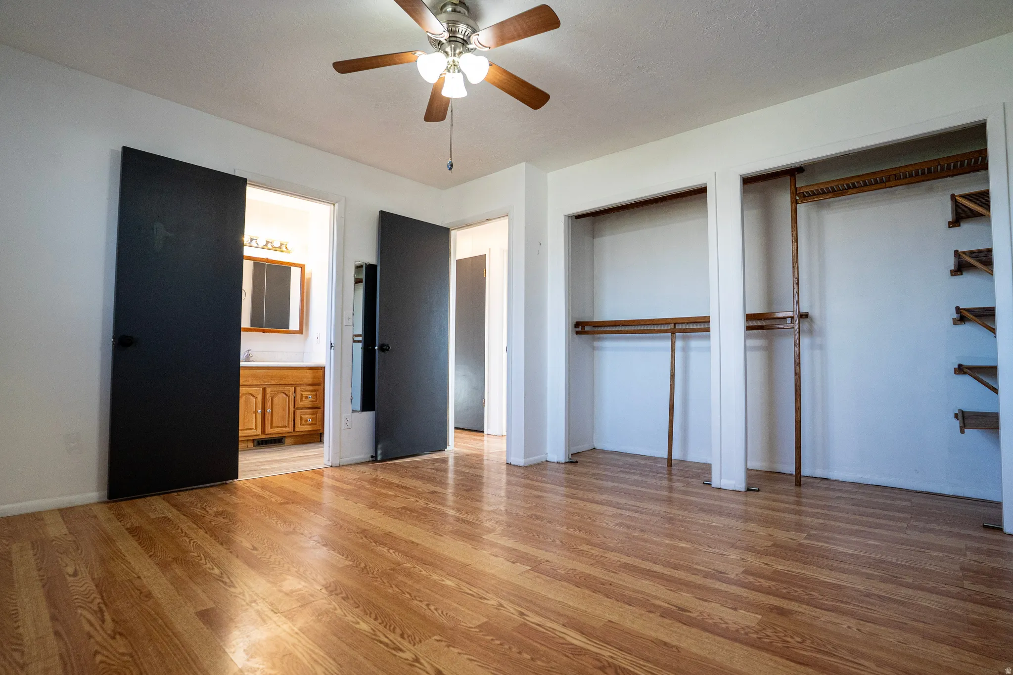 Primary Bedroom (upstairs) with two closets, light wood finished floors, a ceiling fan, and primary bath