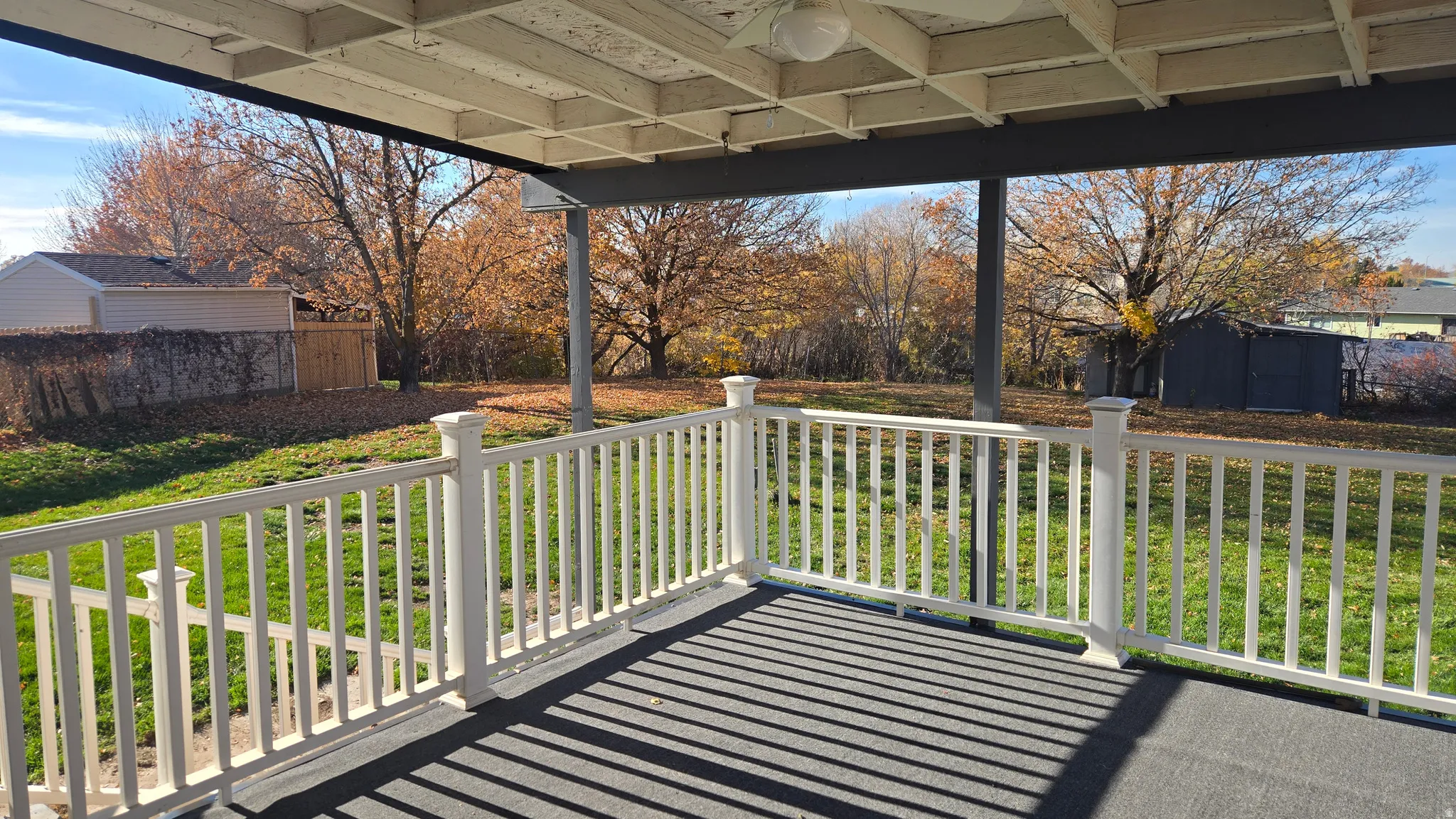 Spacious Covered patio featuring a ceiling fan, fenced backyard with mature trees and outbuildings.