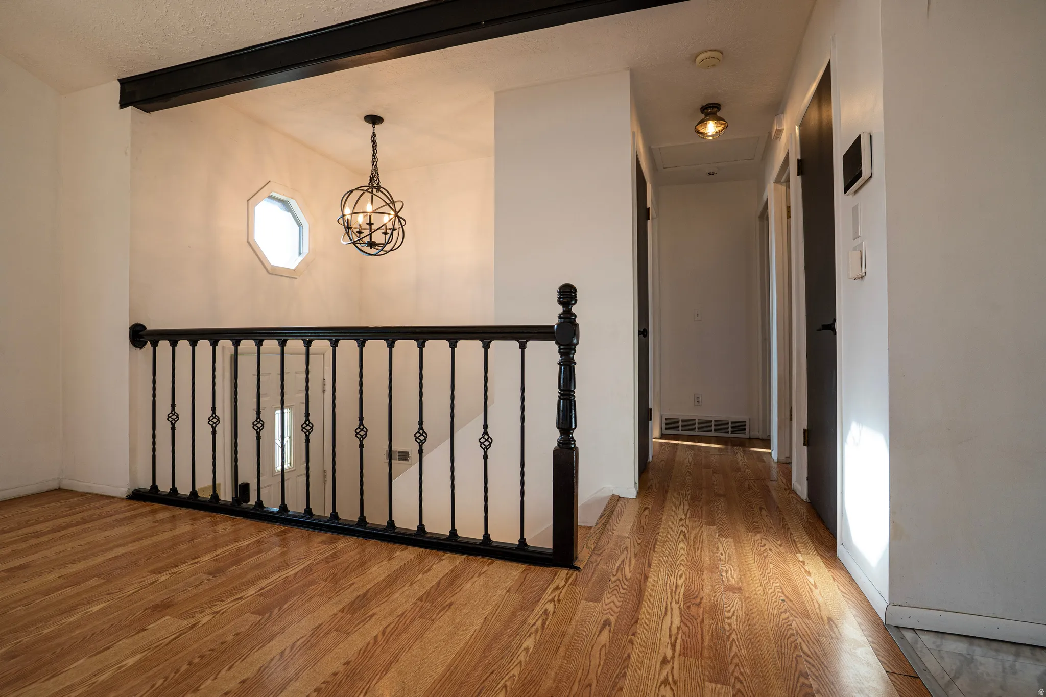 Upstairs hallway featuring wood flooring, a chandelier, and beamed ceiling