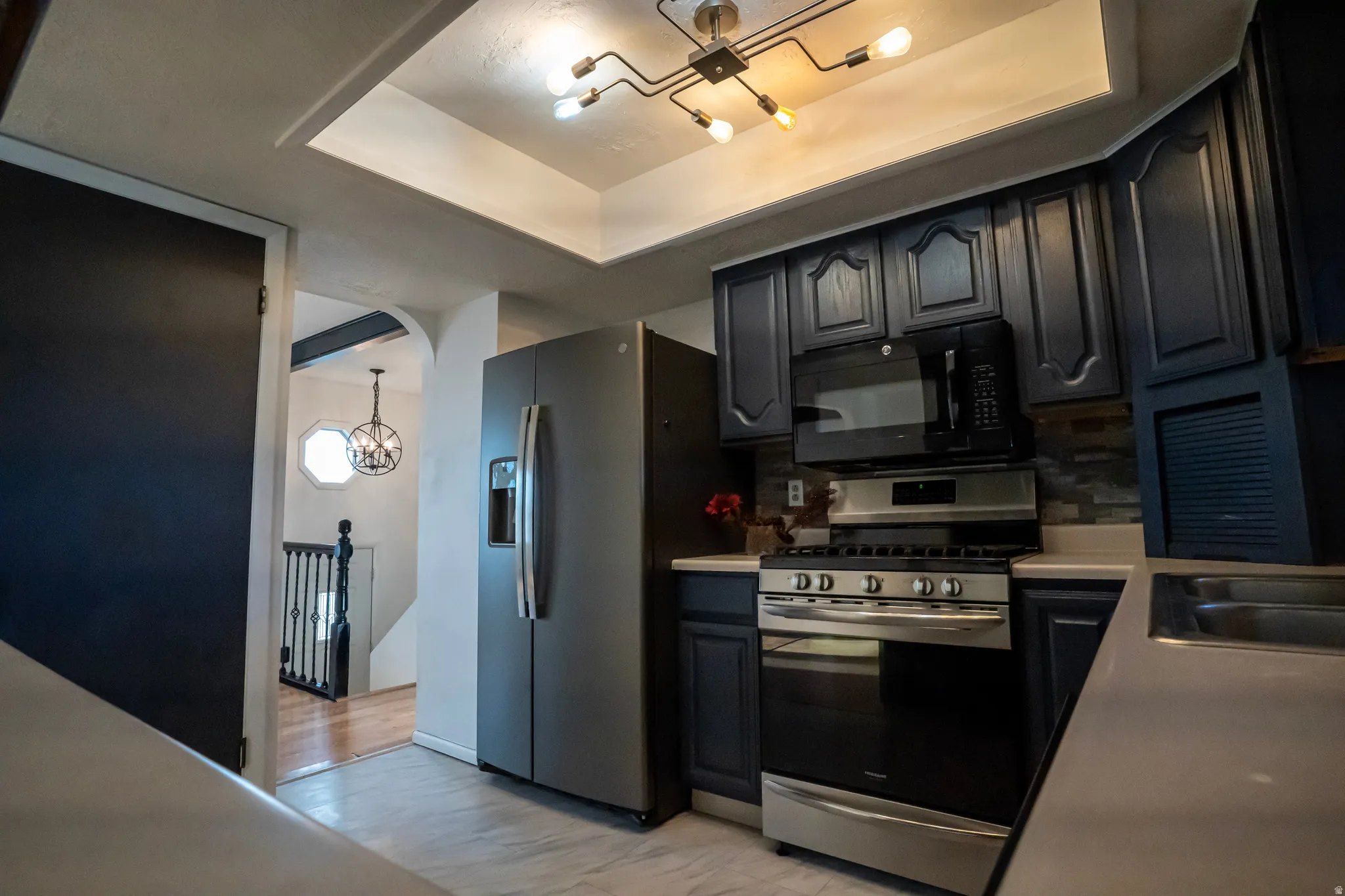 Kitchen featuring a chandelier, appliances with stainless steel finishes, a tray ceiling, light countertops, and backsplash