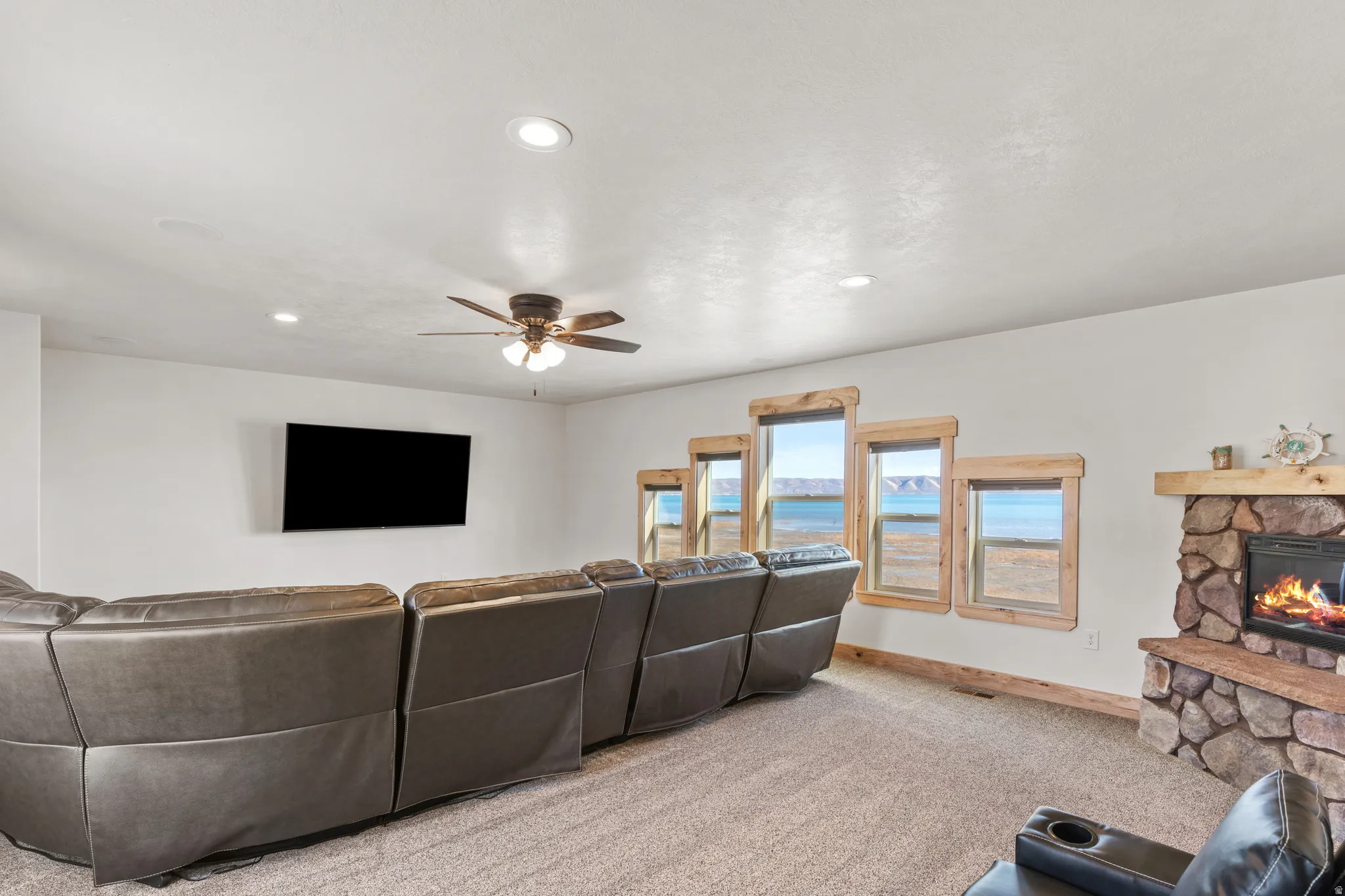 Carpeted living room with a stone fireplace, recessed lighting, and a ceiling fan