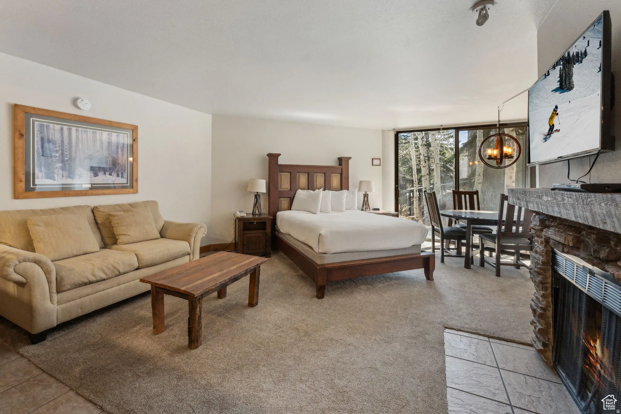 Bedroom with a stone fireplace, a chandelier, a wall of windows, light tile patterned flooring, and light carpet