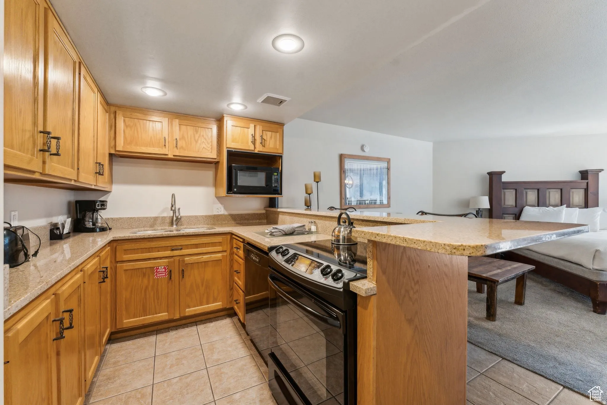 Kitchen with black appliances, light tile patterned floors, a peninsula, light stone counters, and recessed lighting