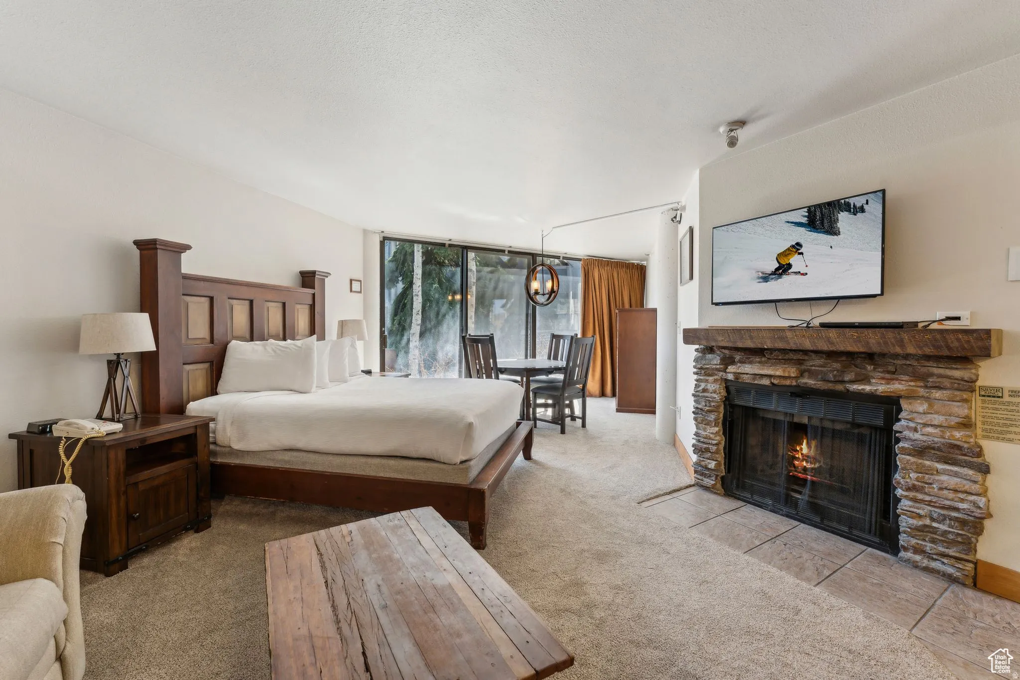 Carpeted bedroom with a stone fireplace, floor to ceiling windows, and a chandelier