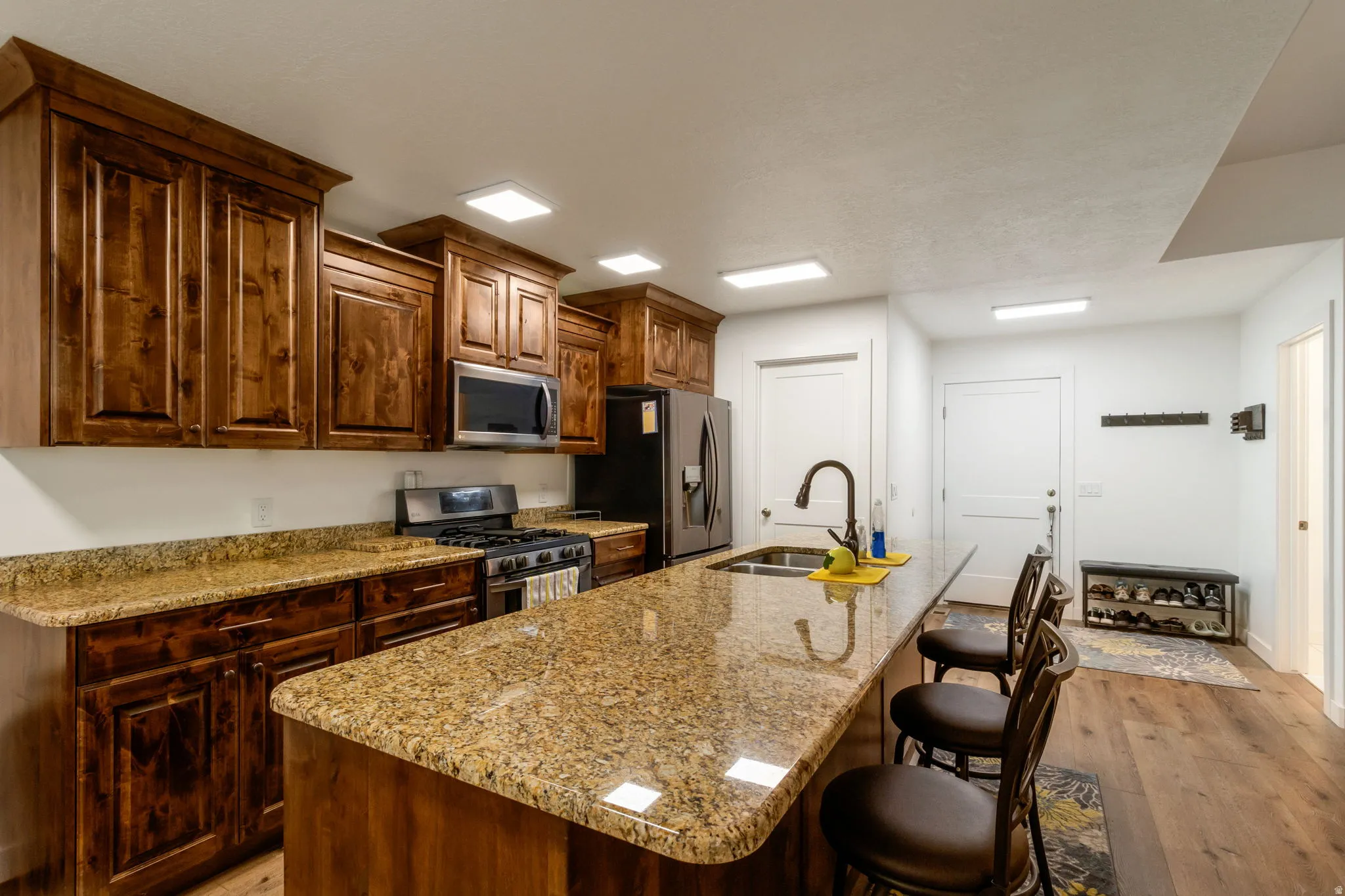 Kitchen with stainless steel appliances, a breakfast bar, light wood finished floors, light stone countertops, and an island with sink