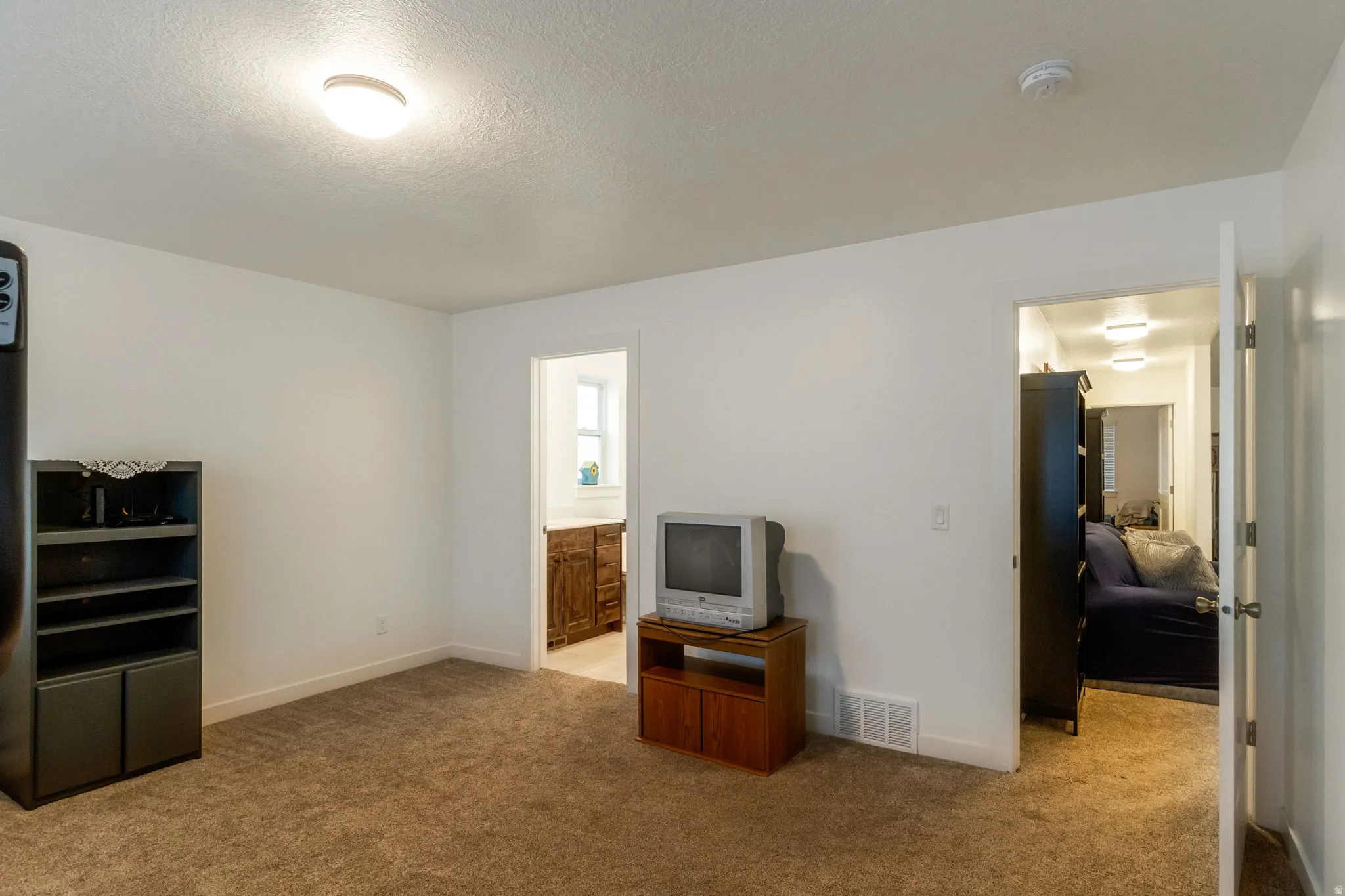 Unfurnished bedroom featuring light carpet, a textured ceiling, and ensuite bath