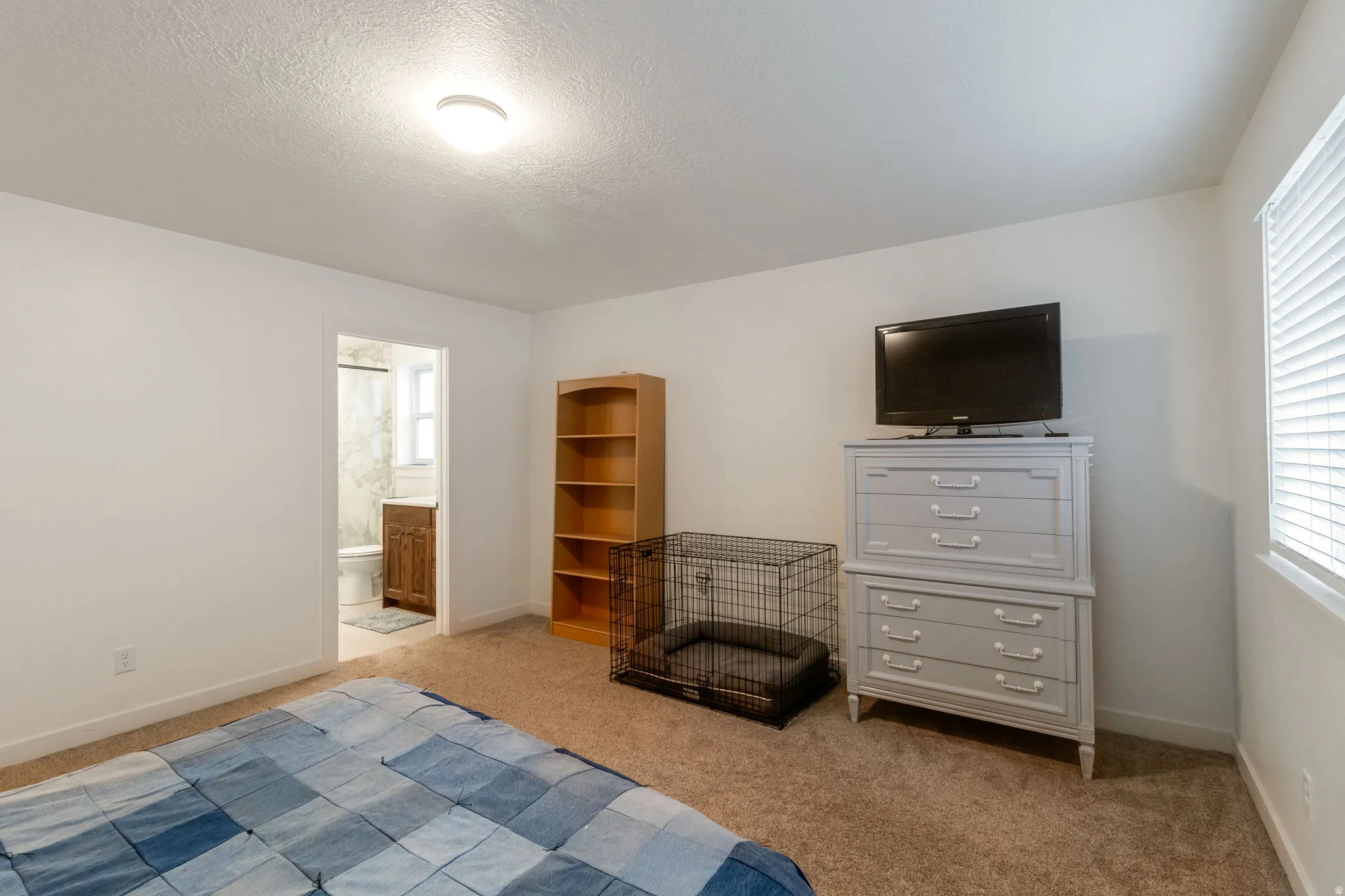 Bedroom with light carpet, multiple windows, a textured ceiling, and connected bathroom