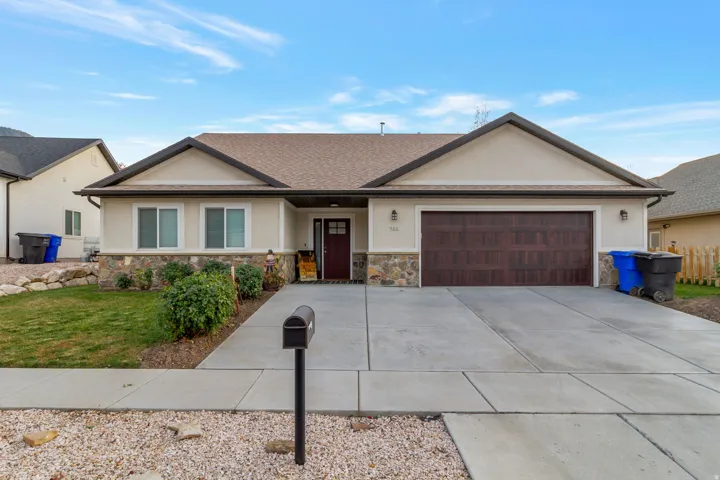 Ranch-style house with stucco siding, a front lawn, a garage, driveway, and stone siding