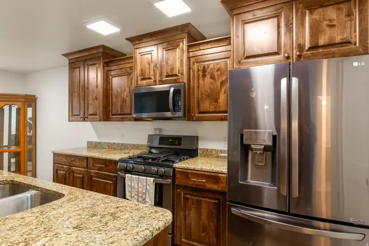 Kitchen featuring appliances with stainless steel finishes, light stone counters, and brown cabinets