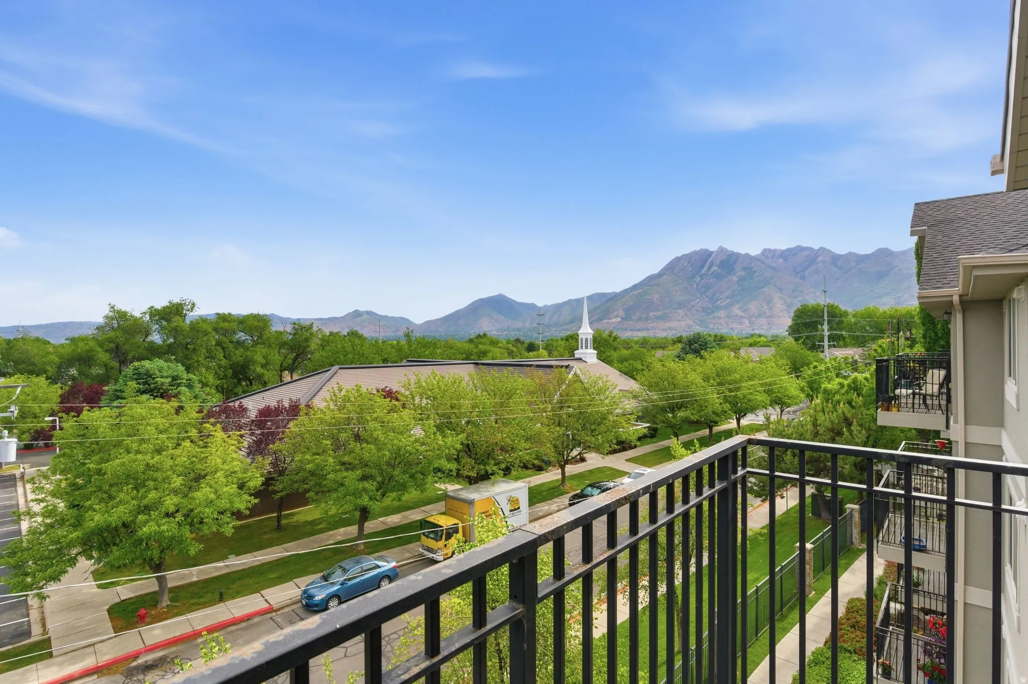 Balcony with black metal railing overlooking a tree-lined street and distant mountains