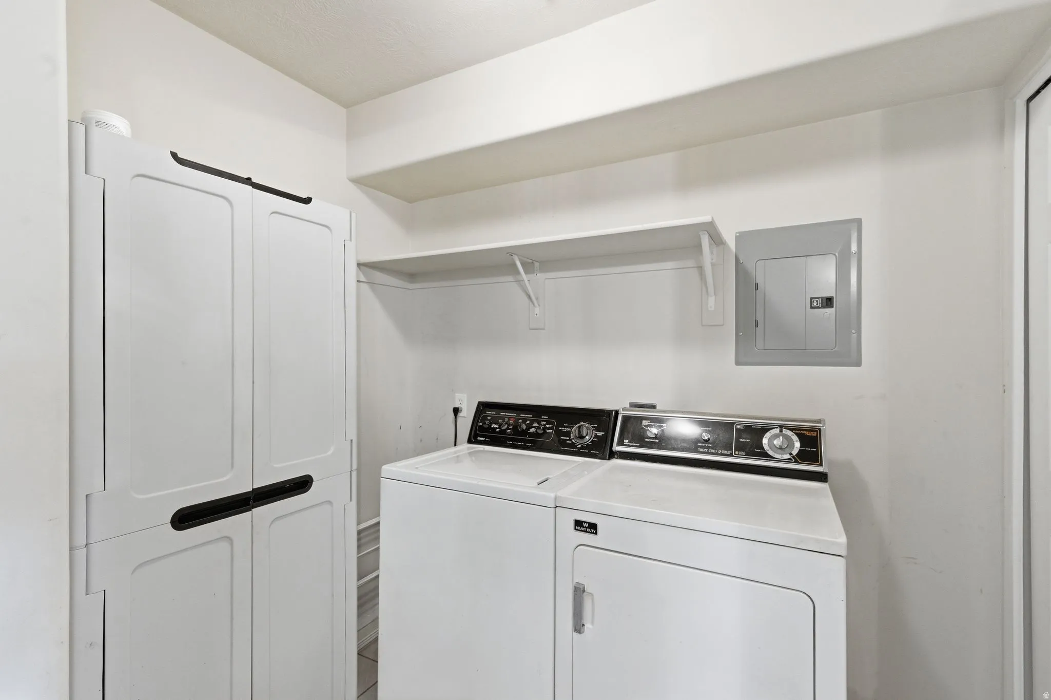 Dedicated laundry room featuring a white storage cabinet with black handles, a white washing machine, and a white dryer