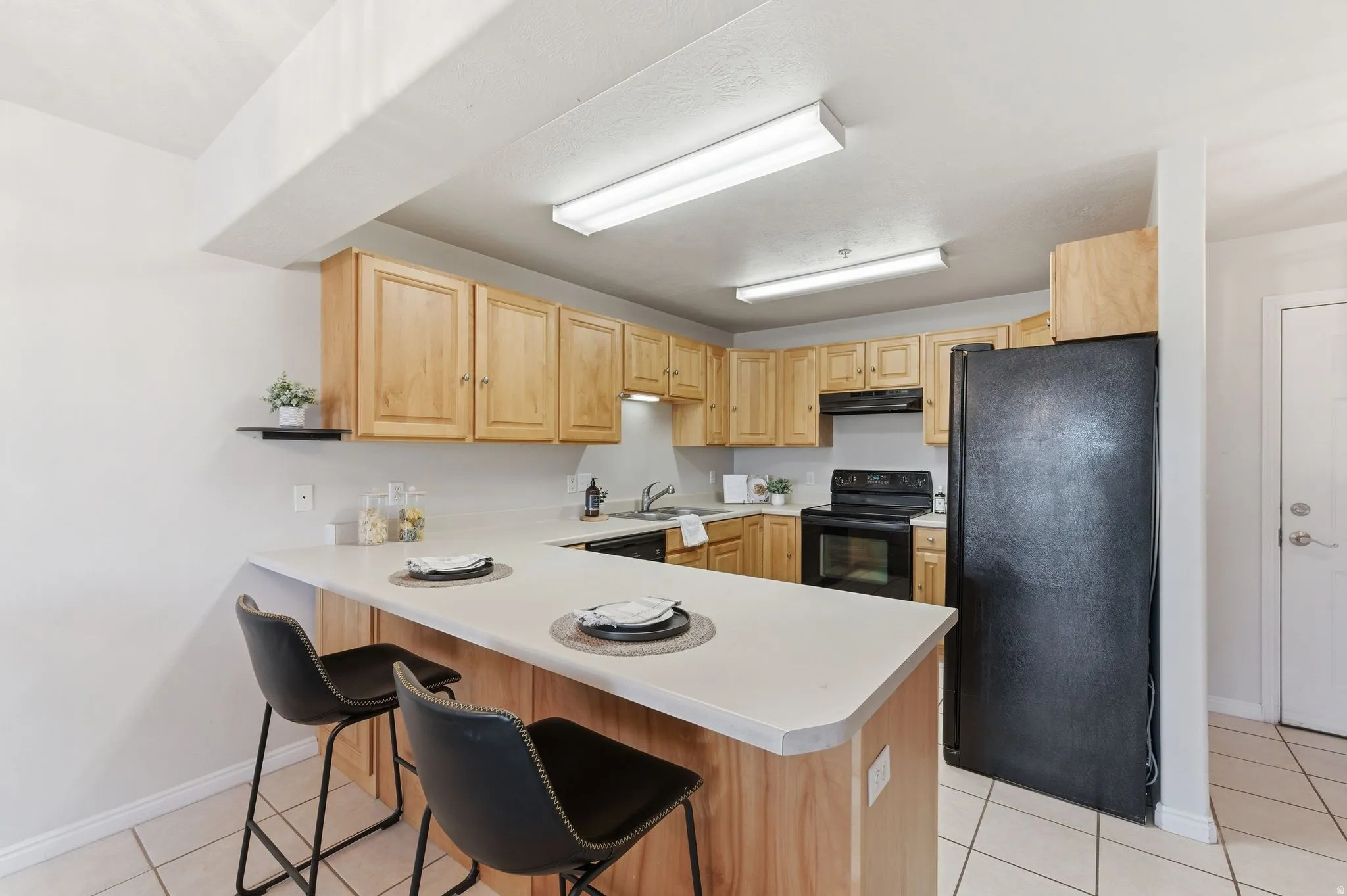Kitchen featuring wood cabinetry, integrated black appliances, light-toned countertops, and a breakfast bar with seating