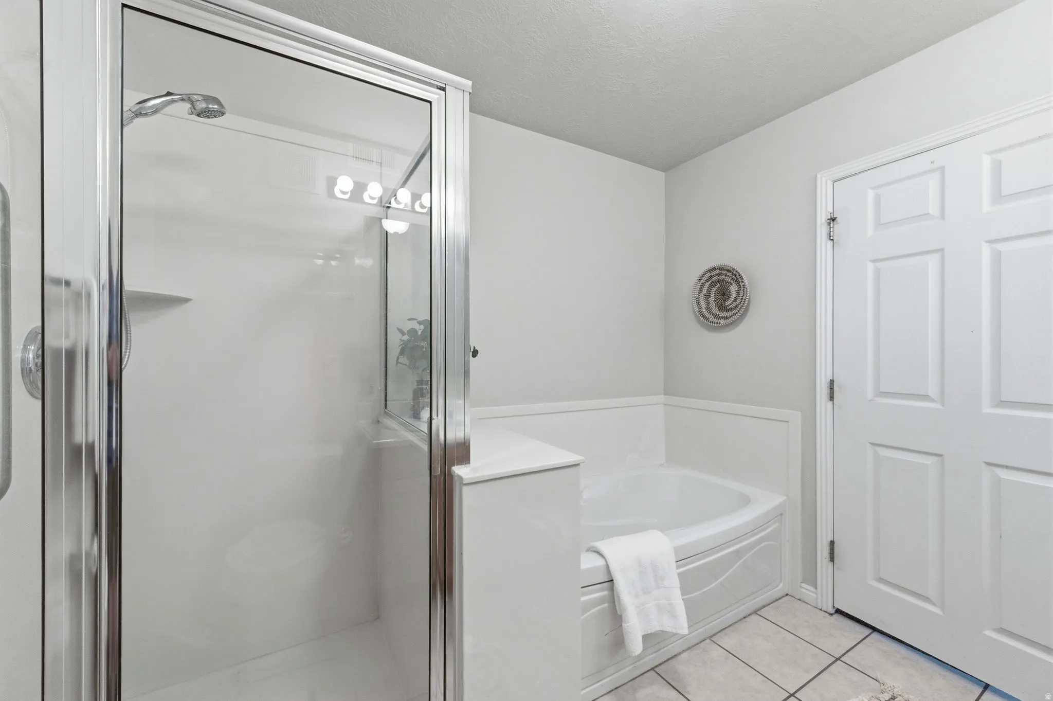Primary bathroom featuring a glass-enclosed shower with chrome fixtures, a built-in corner bathtub, white paneling, and light-toned floor tiling