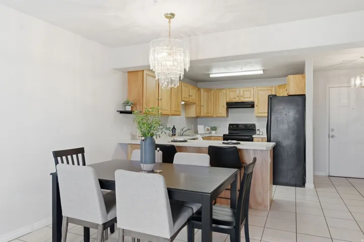 Dining area with a sophisticated crystal chandelier, tile flooring, and a kitchen featuring light wood cabinetry, a breakfast bar, and black appliances