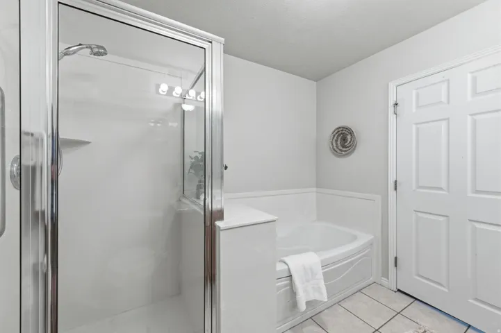 Primary bathroom featuring a glass-enclosed shower with chrome fixtures, a built-in corner bathtub, white paneling, and light-toned floor tiling