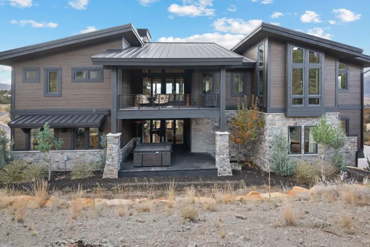Back of house with a standing seam roof, stone siding, a balcony, a metal roof, and a patio area