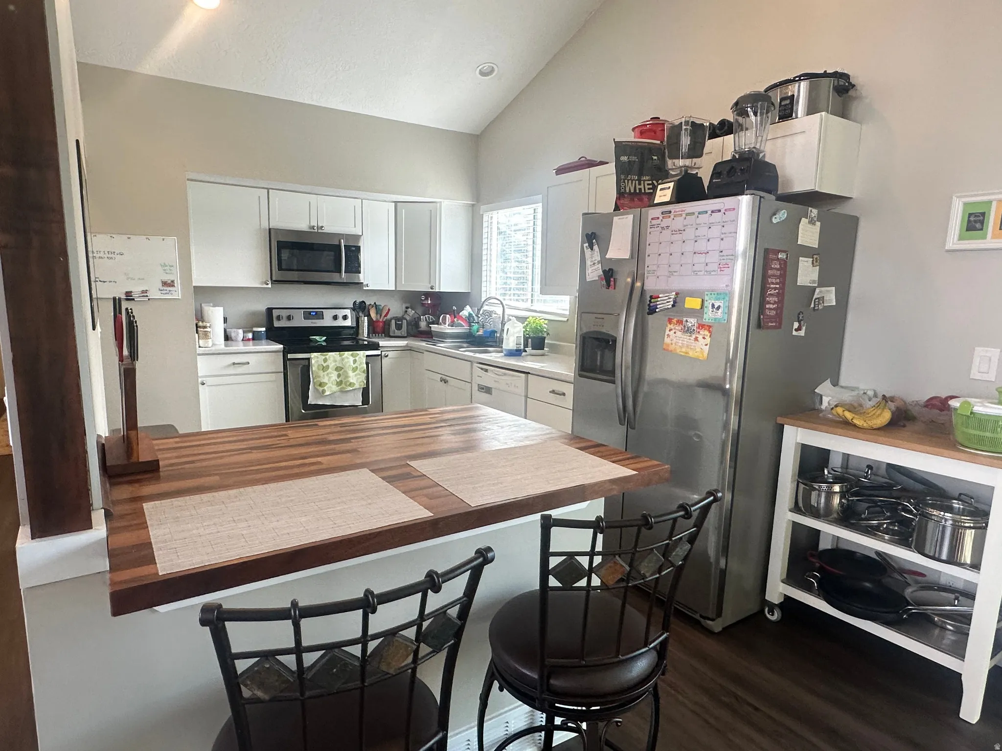 Kitchen with white cabinets, appliances with stainless steel finishes, a breakfast bar area, vaulted ceiling, and dark wood finished floors