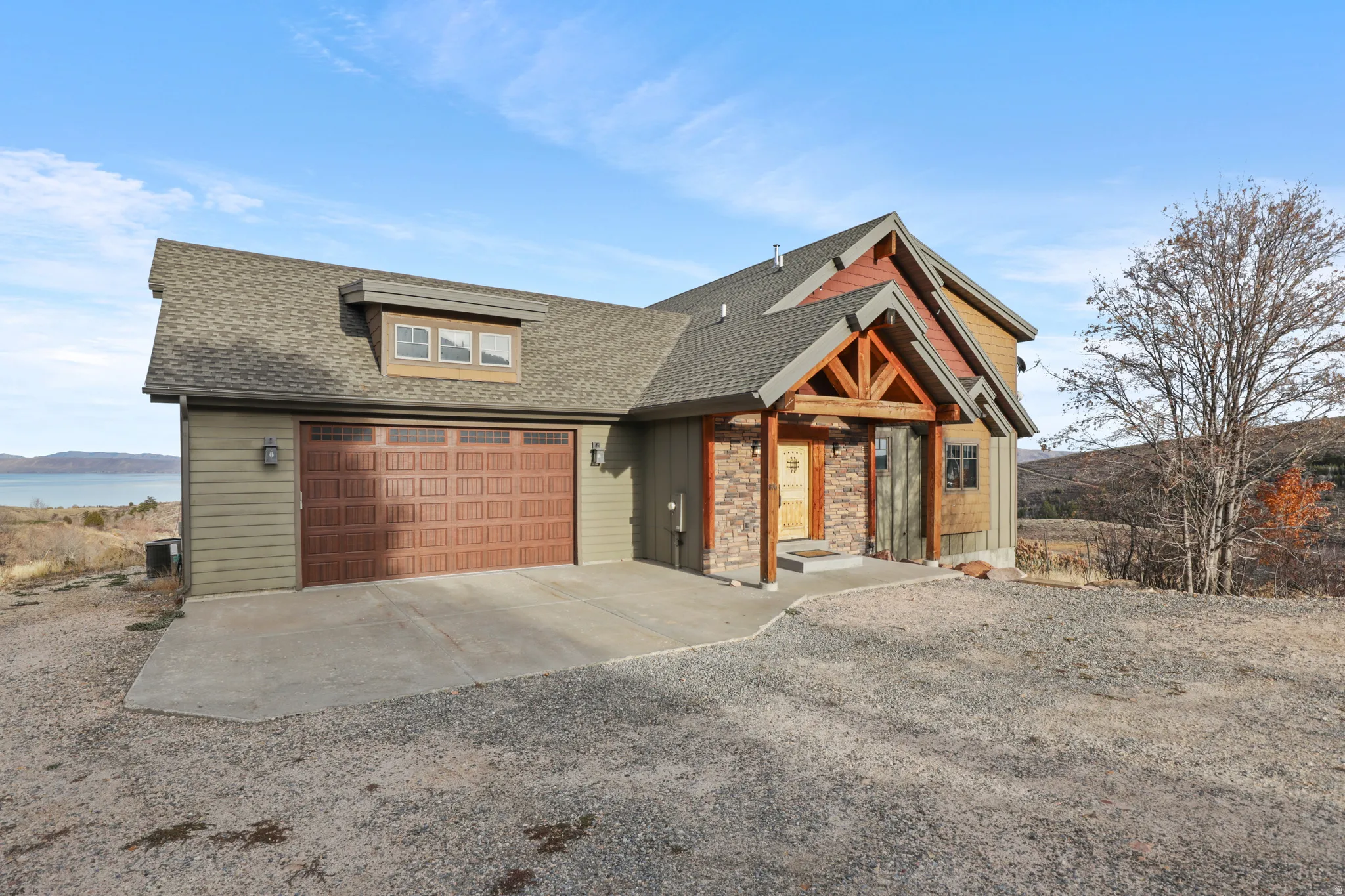 View of front facade featuring a shingled roof, driveway, a water view, and a garage