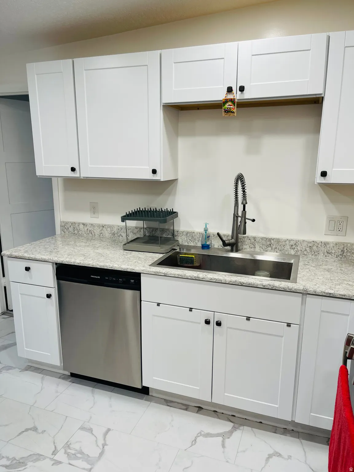 Kitchen with light marble finish floors, stainless steel dishwasher, white cabinets, and light stone countertops