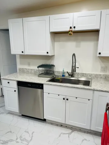 Kitchen with light marble finish floors, stainless steel dishwasher, white cabinets, and light stone countertops
