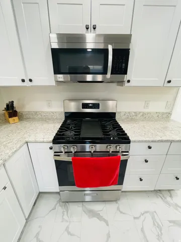Kitchen with stainless steel appliances, light stone counters, white cabinetry, and light marble finish flooring