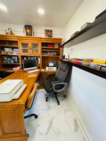 Office featuring a textured ceiling, light marble finish floors, and built in desk