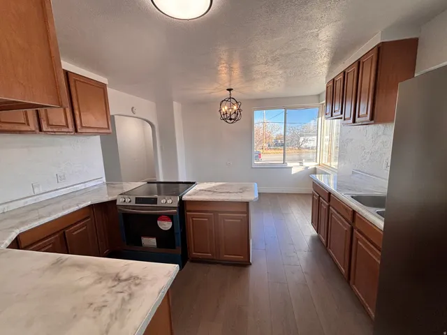 Kitchen featuring appliances with stainless steel finishes, dark wood-type flooring, a peninsula, hanging light fixtures, and brown cabinets
