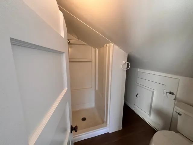Bathroom featuring a shower stall, dark wood-style floors, and vaulted ceiling