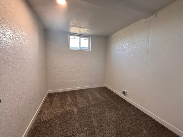Spare room featuring a textured wall, dark colored carpet, and a textured ceiling
