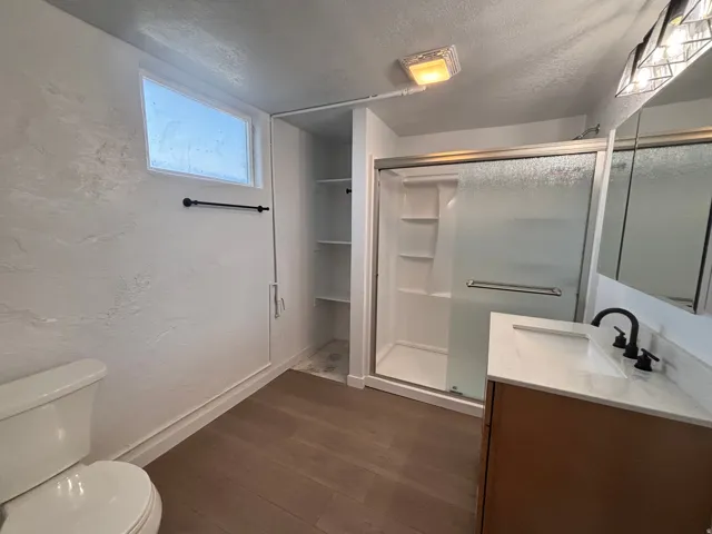Bathroom featuring a textured ceiling, vanity, dark wood-style floors, a stall shower, and a textured wall