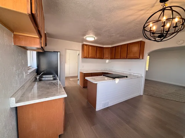Kitchen featuring brown cabinetry, arched walkways, dark wood finished floors, a textured ceiling, and a peninsula