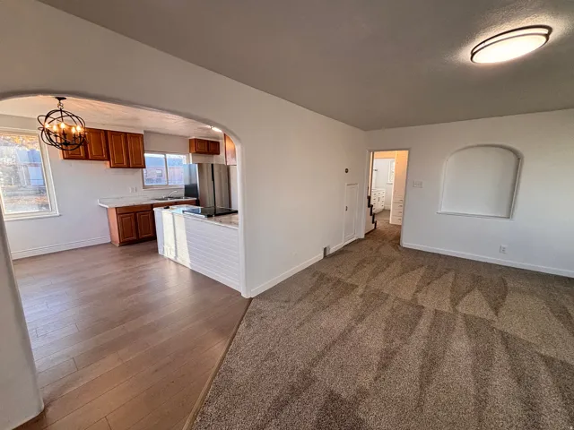 Unfurnished living room featuring arched walkways, a chandelier, dark carpet, and dark wood finished floors