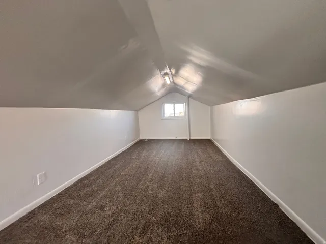 Additional living space featuring dark carpet and vaulted ceiling