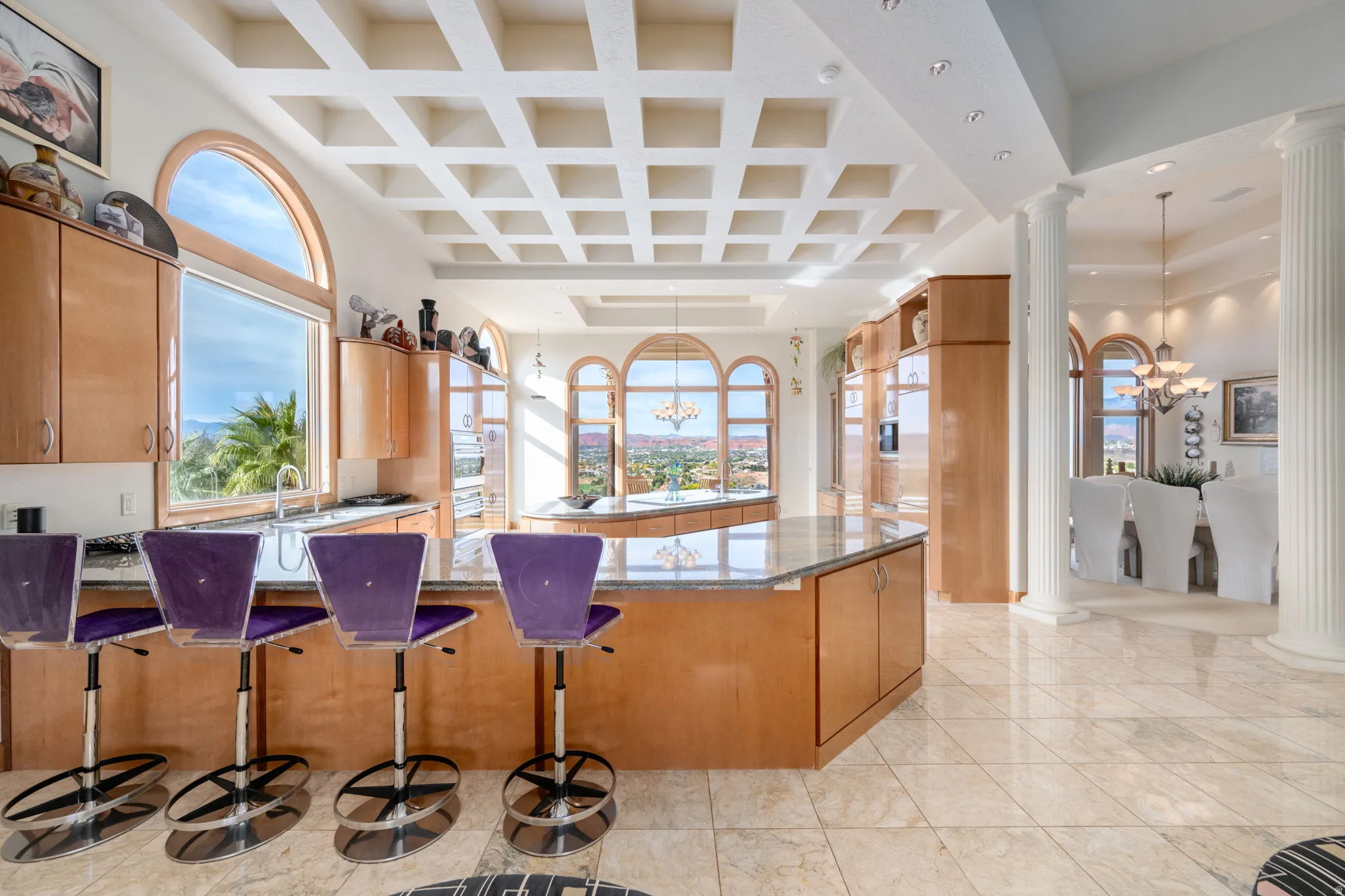Kitchen with a chandelier, dark stone countertops, coffered ceiling, ornate columns, and a kitchen breakfast bar
