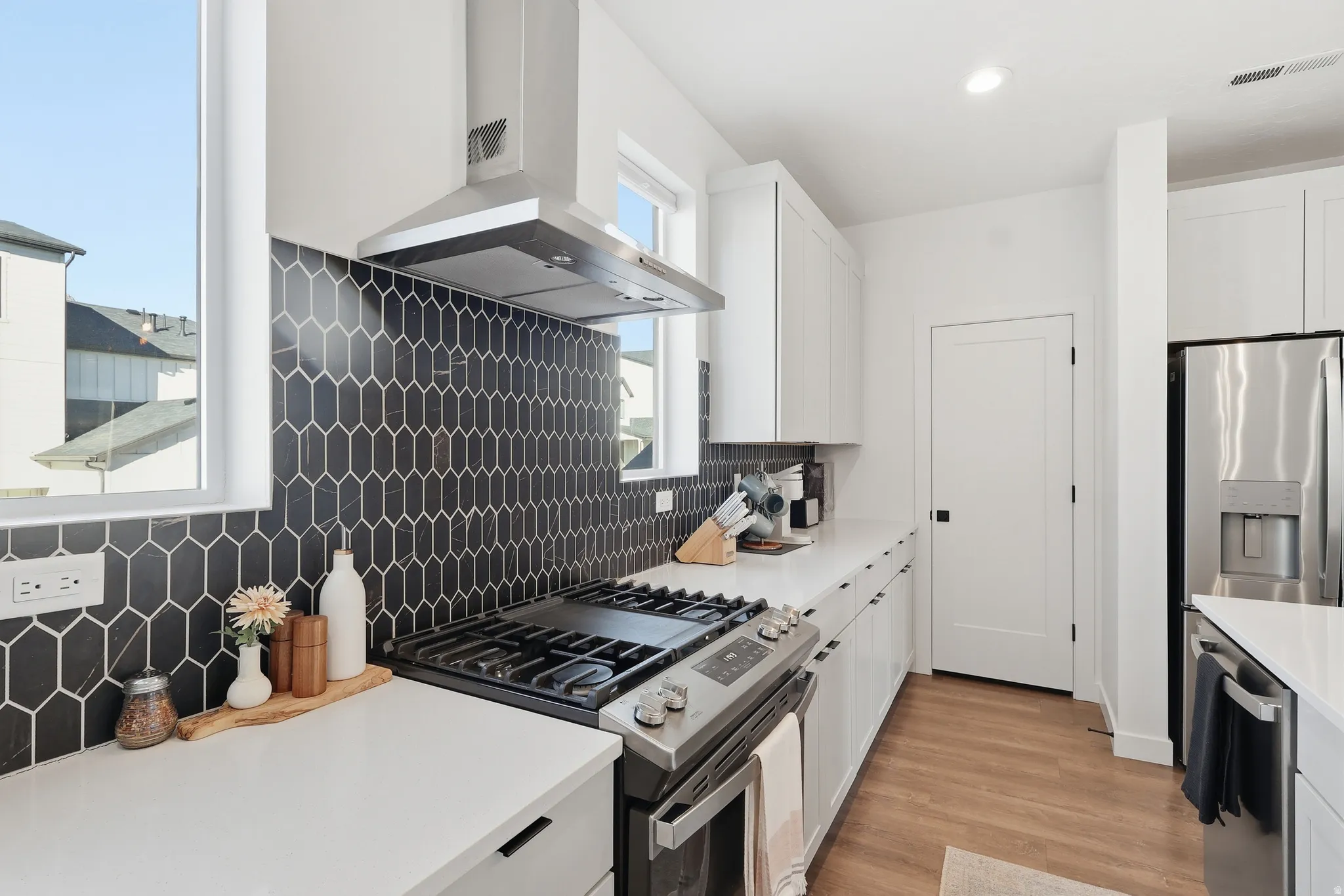 Kitchen with white cabinets, decorative backsplash, range hood, and recessed lighting