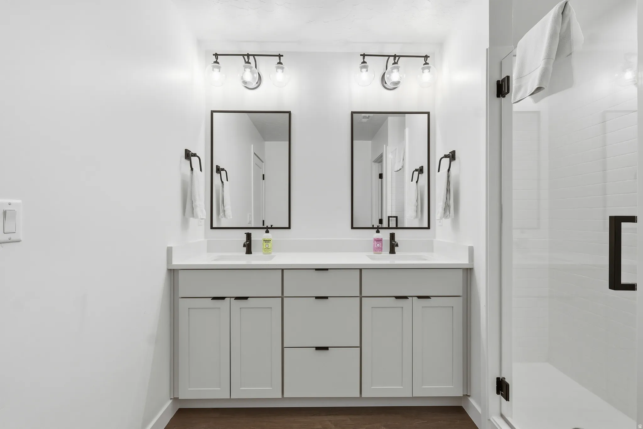 Bathroom featuring double vanity, dark wood-style floors, and a shower stall
