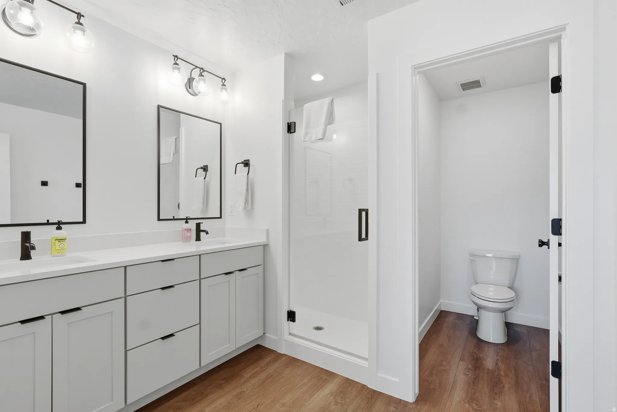 Full bath featuring a stall shower, light wood-type flooring, double vanity, and recessed lighting